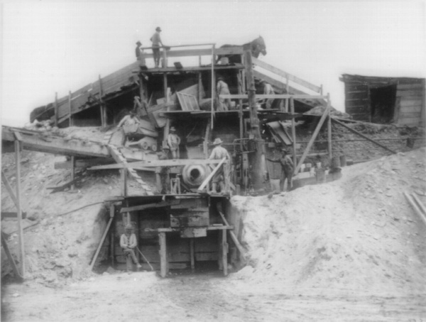 Workers on a multi-level wooden mining structure with machinery and dirt.