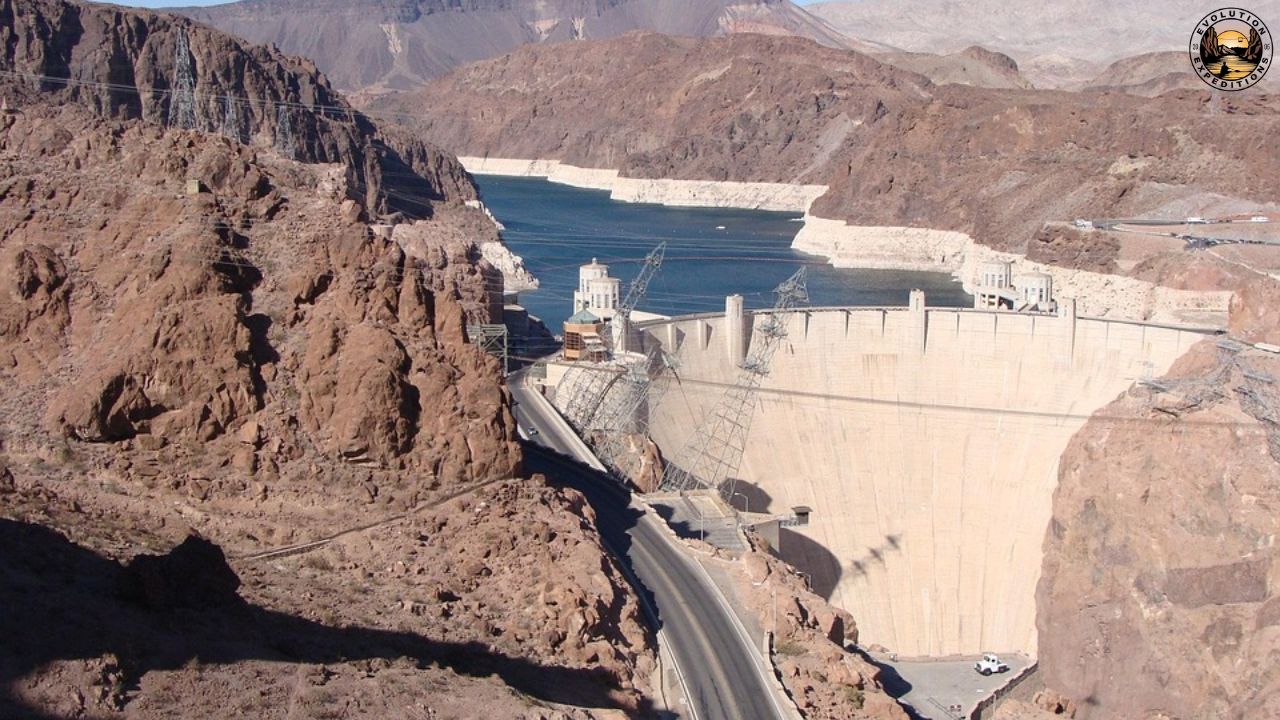 Hoover Dam with reservoir and surrounding rocky landscape under clear sky.