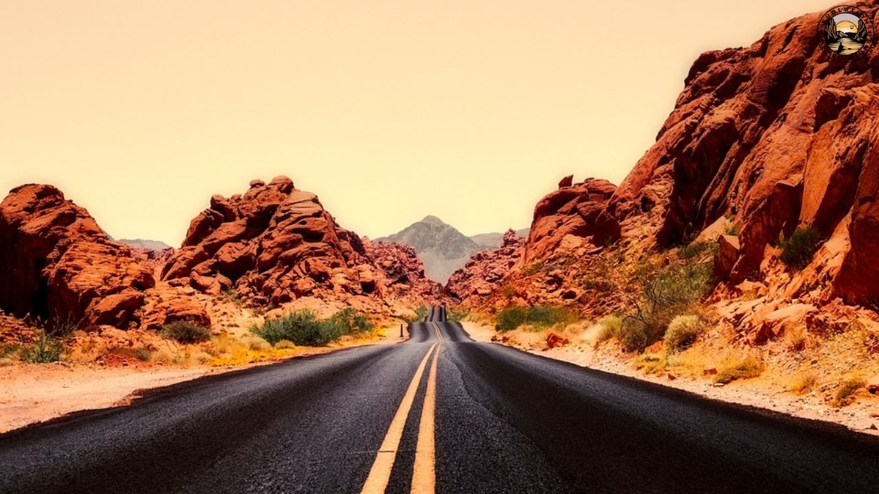 Desert highway flanked by red rock formations under a clear sky.