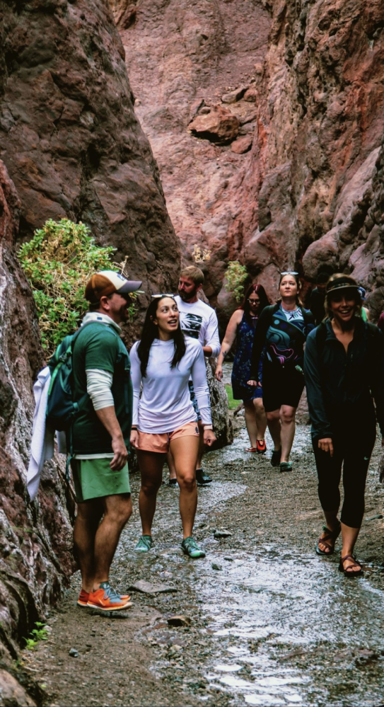 Group of hikers walking through narrow rocky canyon trail.