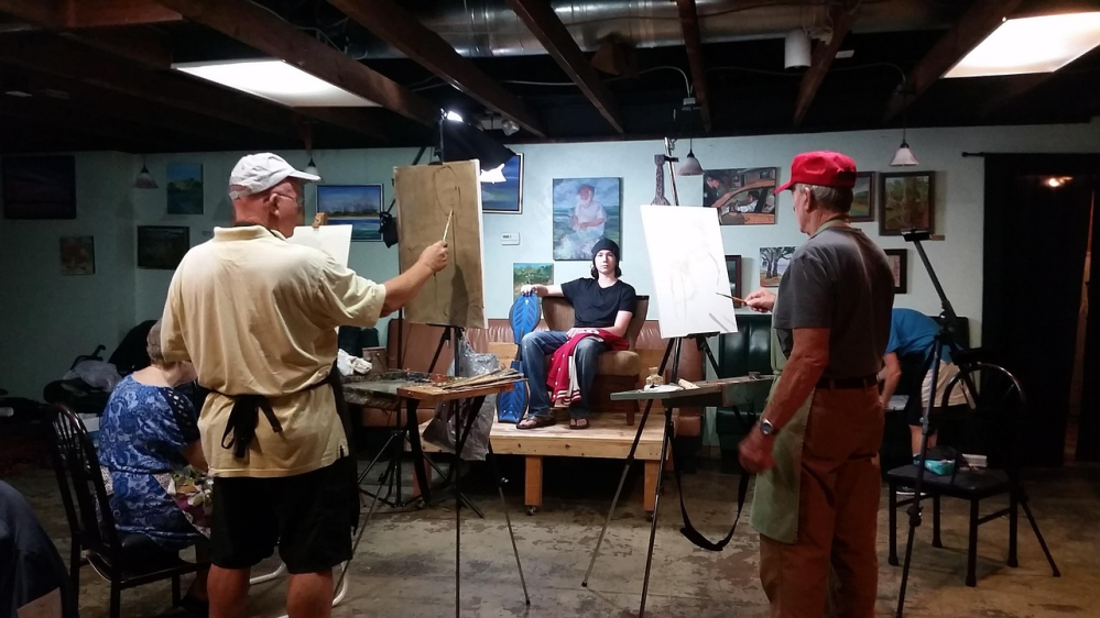 Art class with two artists painting a seated model in a studio.
