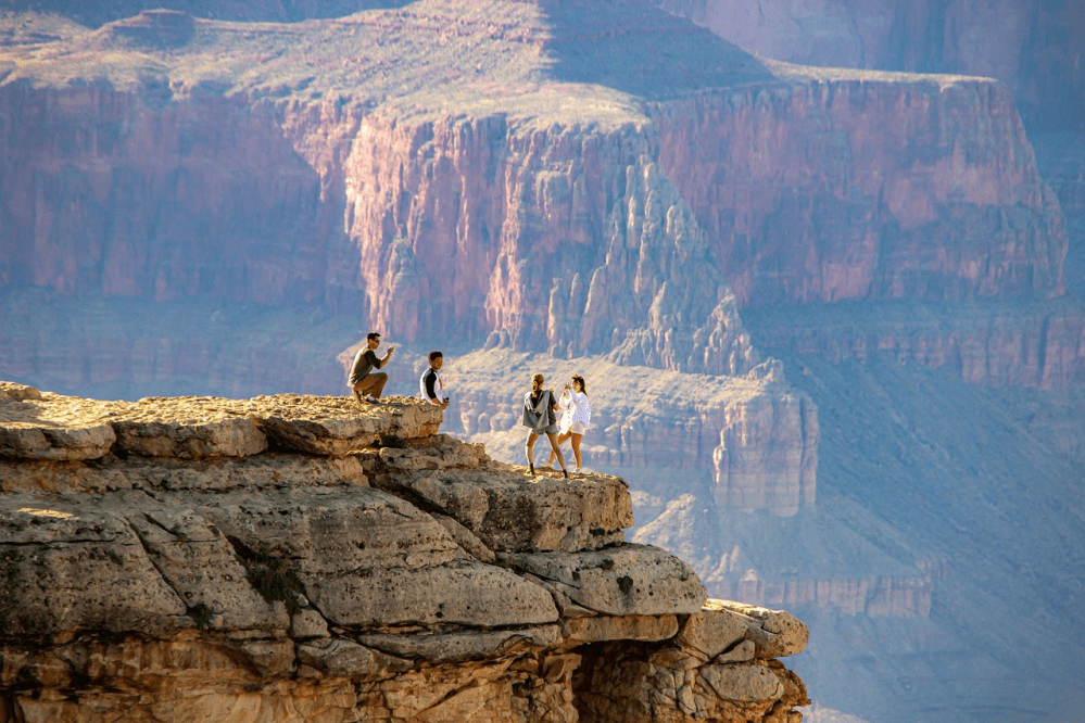 Four people on a cliff edge with a vast canyon backdrop in the distance.