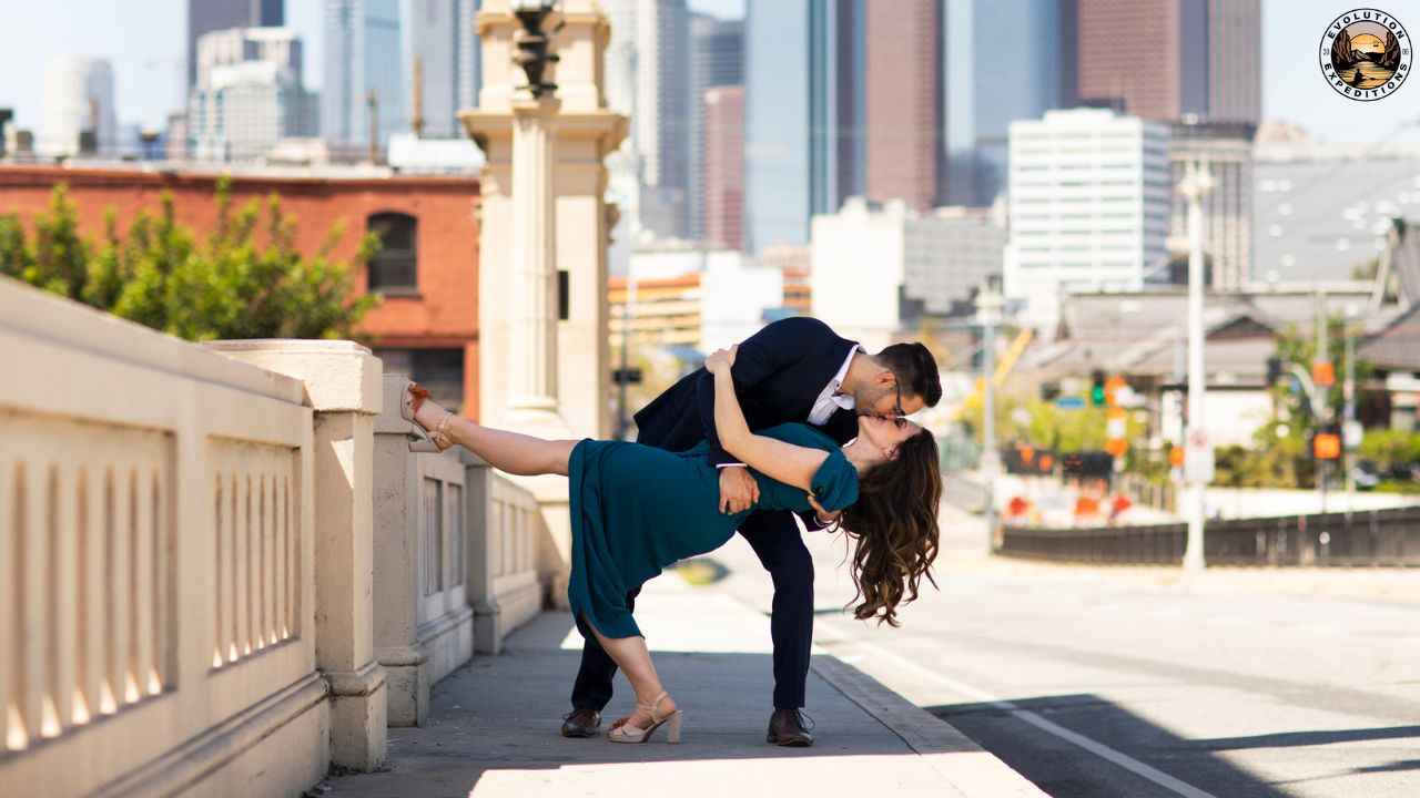 Couple dancing and kissing on a city bridge with skyline in background.
