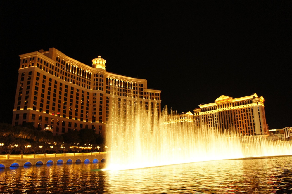 Illuminated fountain at night with lit-up hotel buildings in the background.