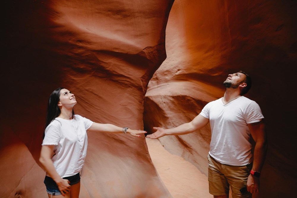 Two people in white shirts admire sandstone walls in a narrow canyon.