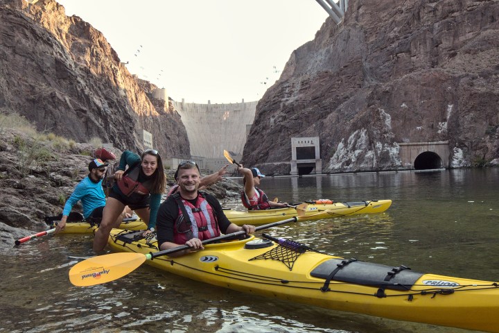 Group kayaking near a dam with a large bridge in the background.
