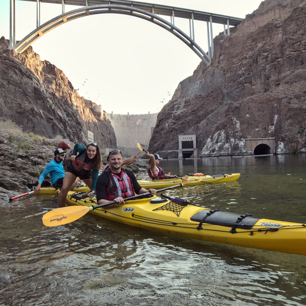 Group kayaking near a dam with a large bridge in the background.