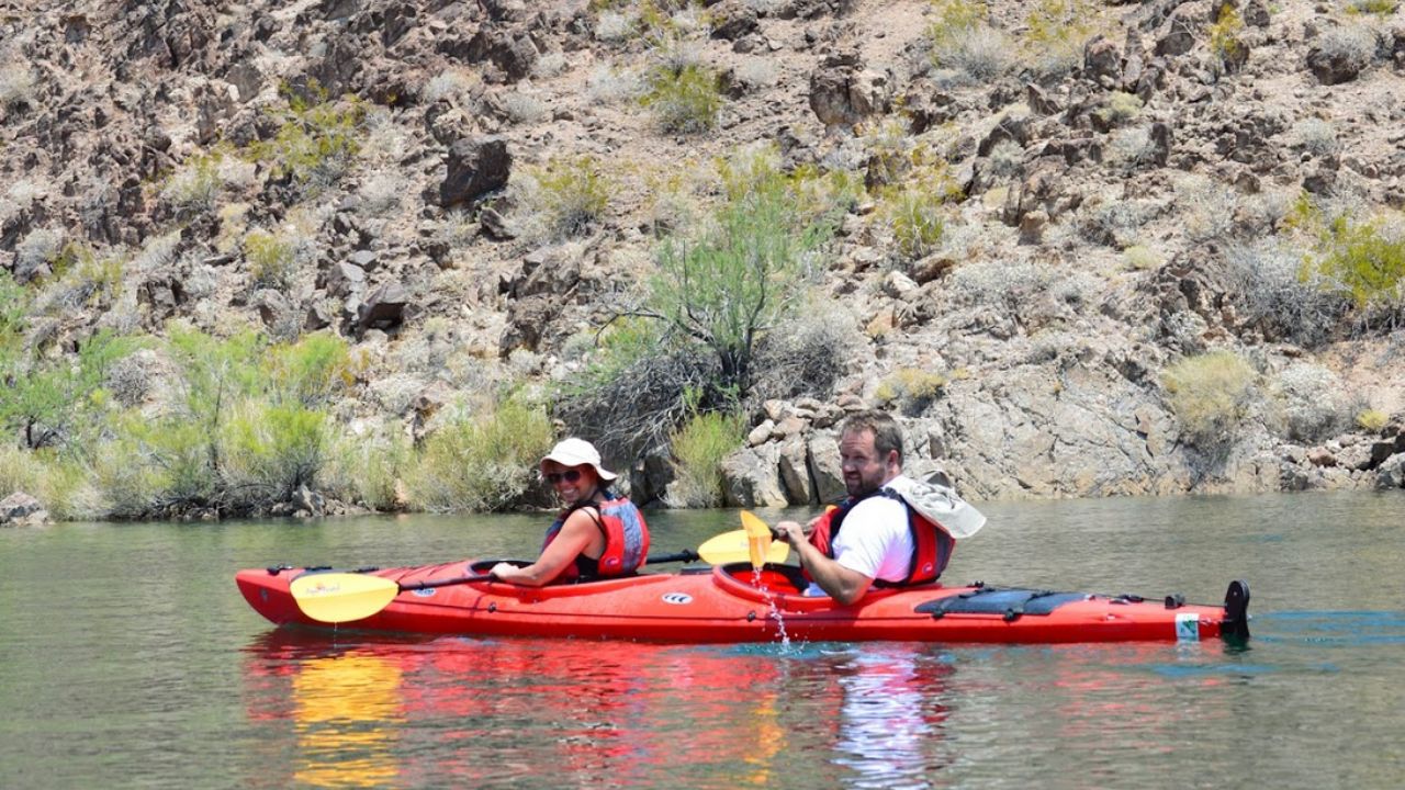 Two people paddle a red tandem kayak on calm water in Black Canyon.