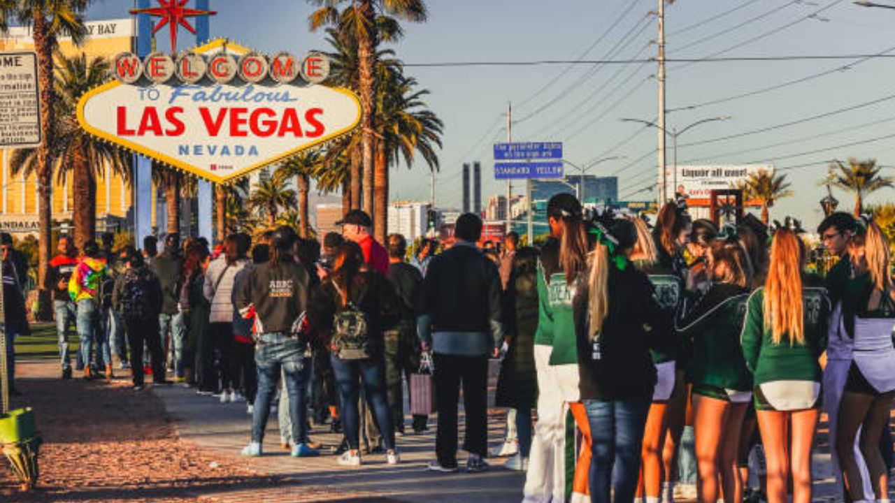 Crowd in front of the Welcome to Las Vegas sign, sunny day with palm trees.