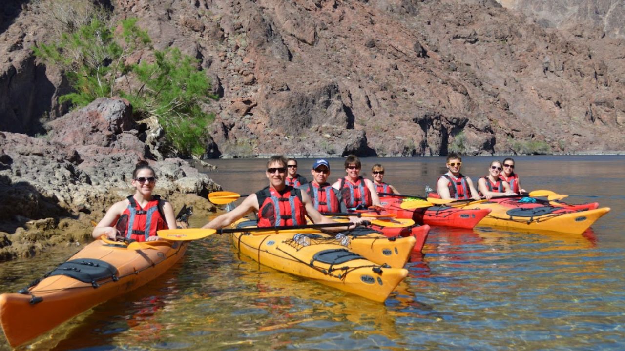 Group kayaking in colorful kayaks on calm water with rocky cliffs in the background.