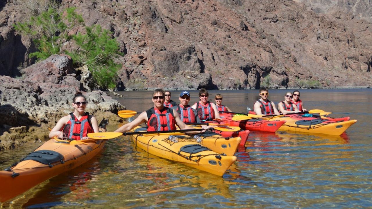 Group kayaking on a calm river with rocky cliffs in the background.