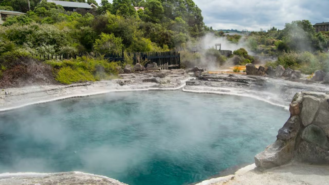Steaming natural geothermal hot spring pool surrounded by rock formations and greenery,