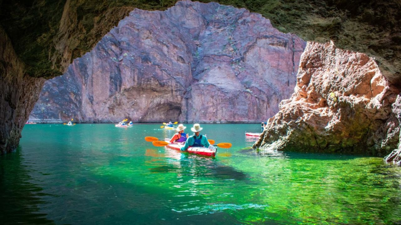 Kayakers paddling through Emerald Cave with glowing green water as part of Evolution Expeditions tour.