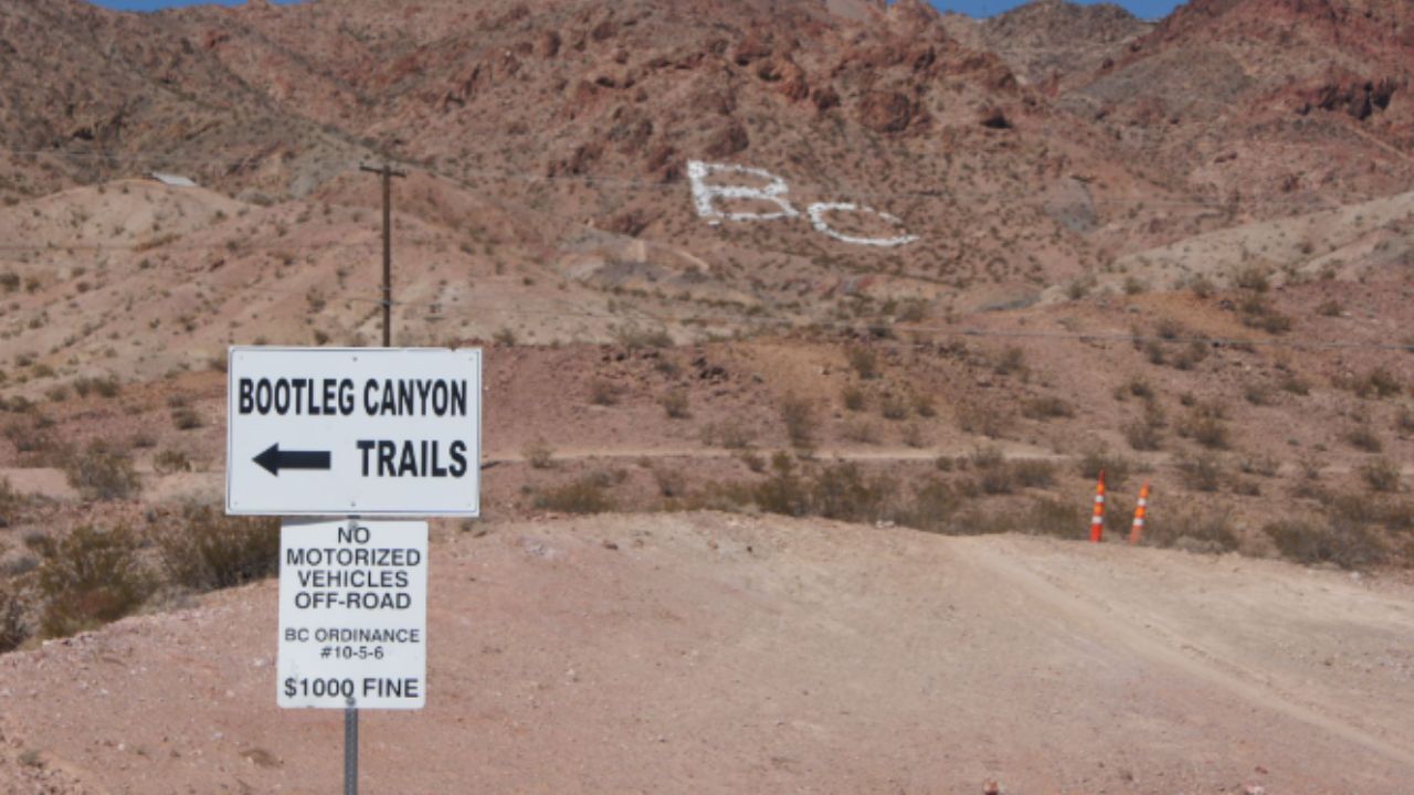  Entrance sign for Bootleg Canyon Trails in a desert landscape with rocky hills and trail access road.