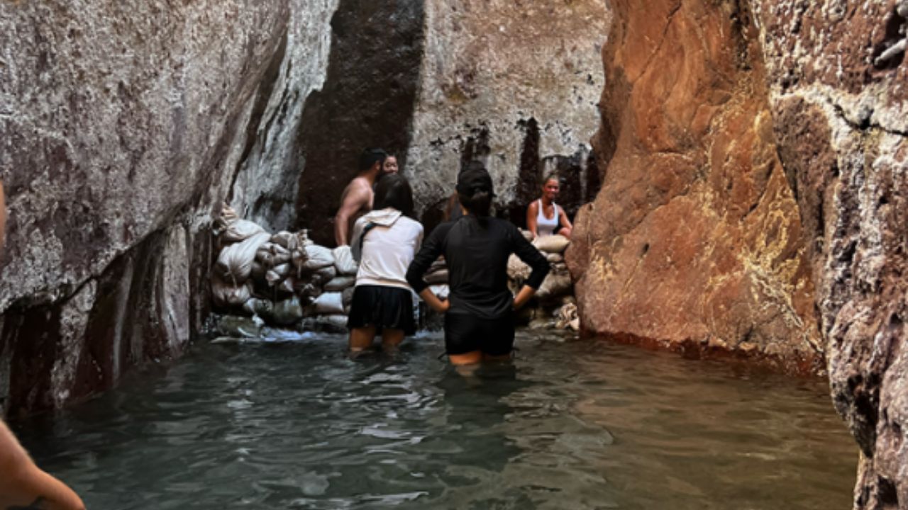 People wading through warm water inside a narrow canyon hot spring as part of Evolution Expeditions tour.