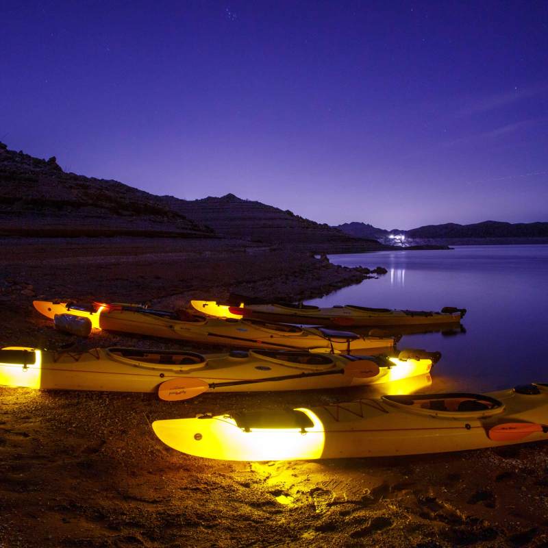 Yellow kayaks with lights rest on a lakeshore at dusk.