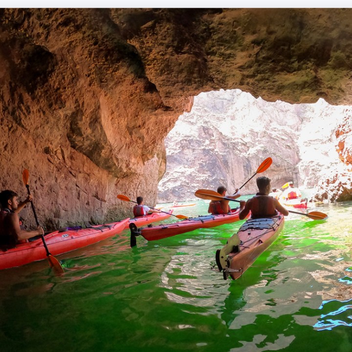 People kayaking through a cave with sunlight in the background.