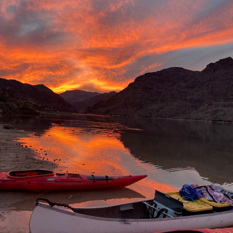 Sunset over a lake with kayaks and mountains in the background.