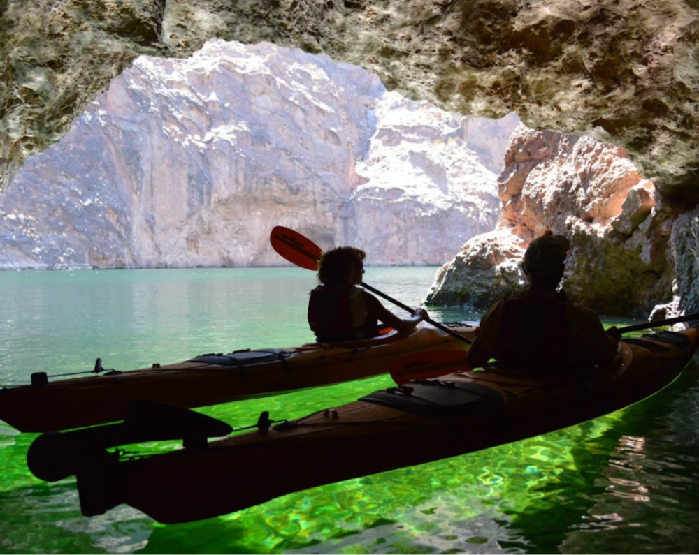 Kayakers inside Emerald Cave on glowing green water during a guided tour by Evolution Expeditions.