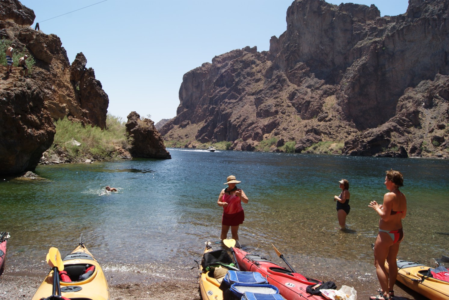 Kayakers paddling through bright green water inside a shaded Black Canyon opening as part of the Evolution Expeditions Emerald Cave tour.