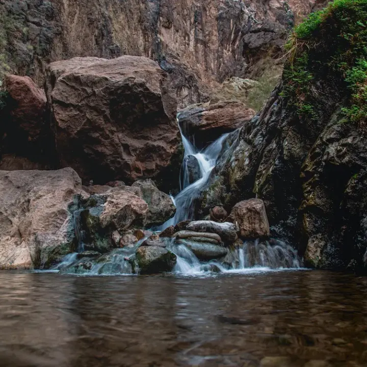 Small waterfall cascading over rocks into a calm pool in a rocky landscape.