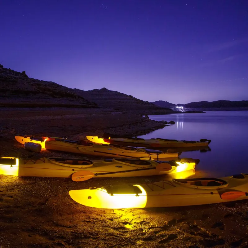 Glowing kayaks on a calm lake at night with a starry sky.