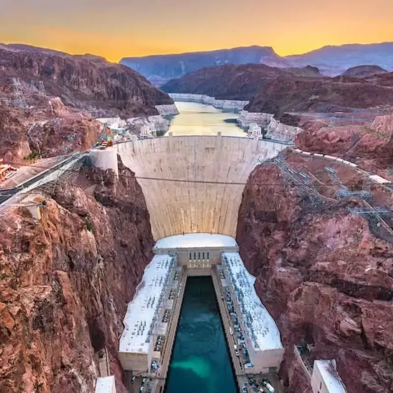 Aerial view of a large dam in a canyon at sunset.
