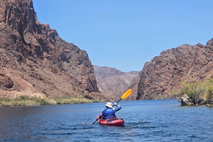 Person kayaking on a calm river between rocky cliffs under a clear blue sky.