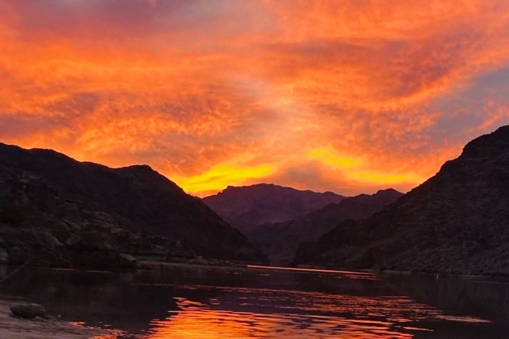 Red kayak on lake at sunset with vibrant orange sky and mountains.