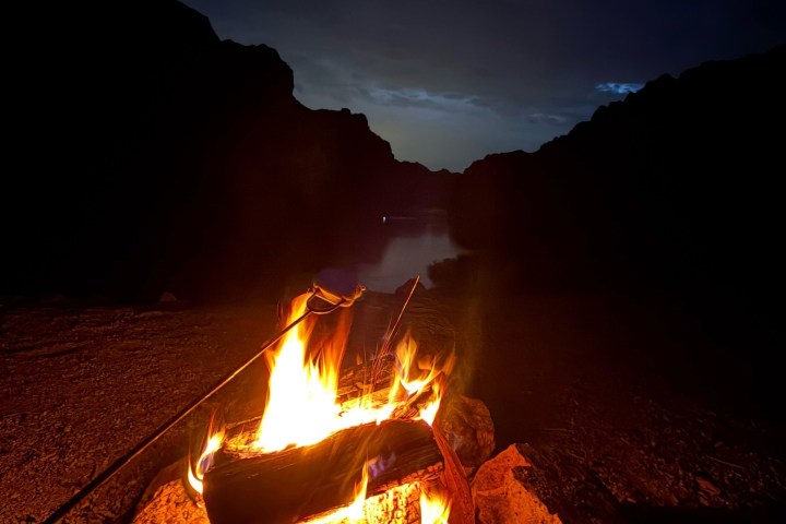 Campfire burning with rocky landscape in the background at dusk.