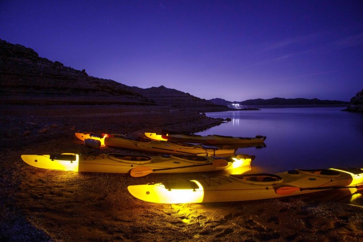Glow-in-the-dark kayaks on a beach by a calm lake at night, with a purple twilight sky.