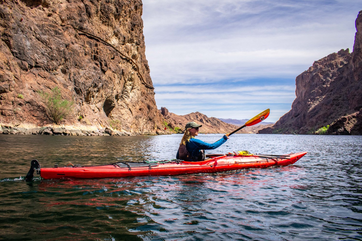 Person kayaking on a river between rocky cliffs on a sunny day.